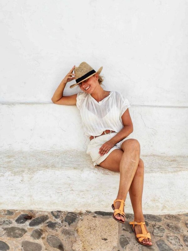 Kobieta w jasnym letnim stroju i słomkowym kapeluszu relaksuje się, siedząc na białej ławce w urokliwej uliczce Minorki.