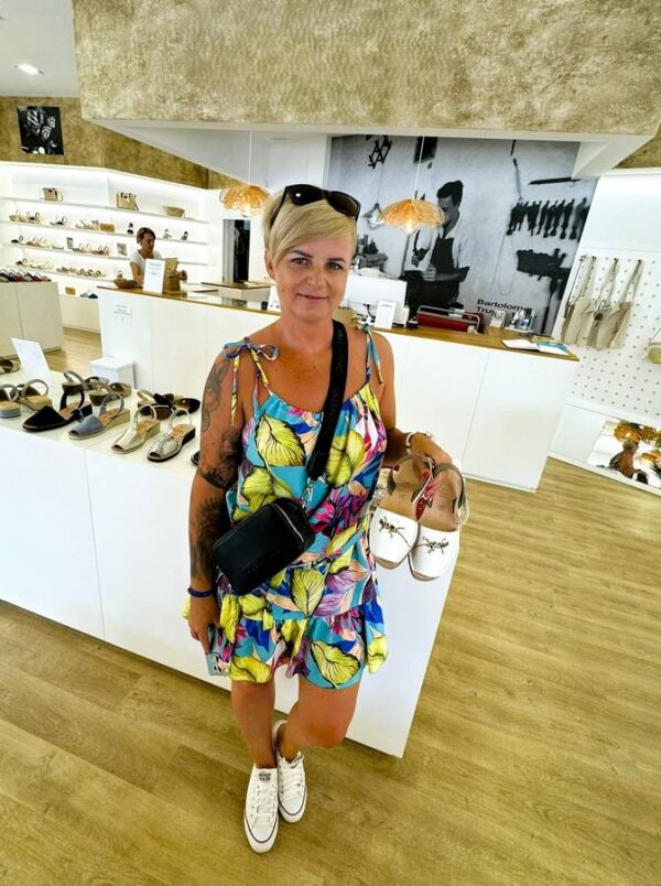 Turystka w sklepie na Minorce prezentuje ręcznie robione sandały avarcas – lokalne rzemiosło i popularna pamiątka z Balearów.