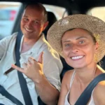 Uśmiechnięta kobieta w słomkowym kapeluszu i mężczyzna w lnianej koszuli w samochodzie, gotowi na wakacyjną przygodę.