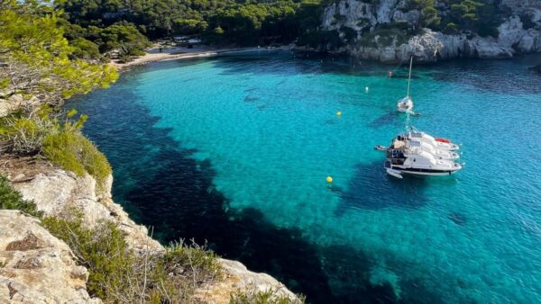 Malownicza zatoka na Minorce z krystalicznie czystą wodą, białymi klifami i zacumowanymi łodziami pod błękitnym niebem