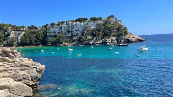 Malownicza zatoka na Minorce z krystalicznie czystą wodą, białymi klifami i zacumowanymi łodziami pod błękitnym niebem