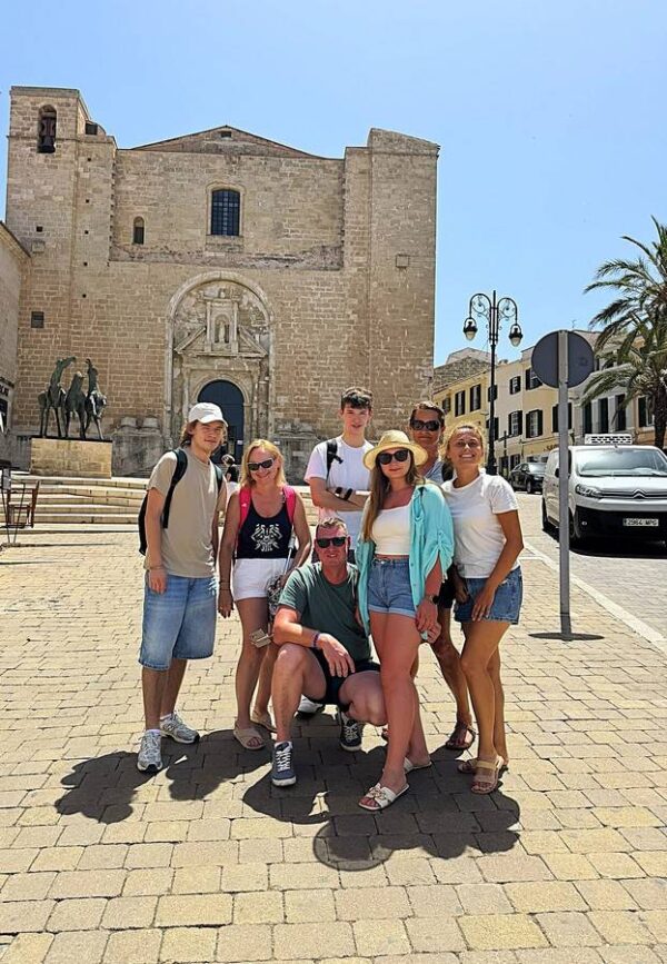 Grupa turystów zwiedzająca Ciutadellę na Minorce, na tle zabytkowego kościoła.