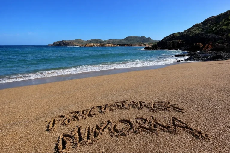 Piaszczysta plaża na Minorce z napisem „Przystanek Minorka” i spokojnym morzem